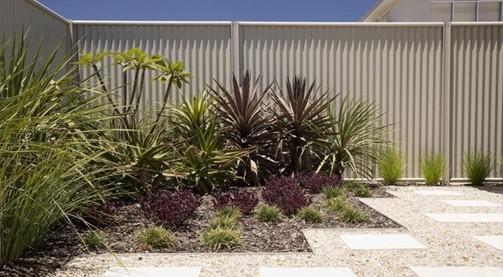 Dark Colorbond steel fence behind a planted garden bed with gravel and paving