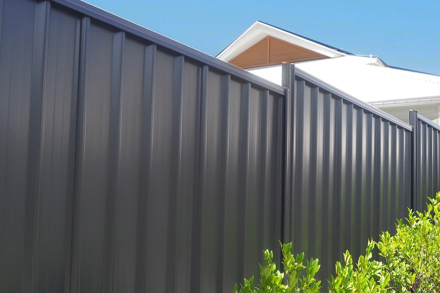 Dark Colorbond steel fence running alongside a house with planting at its base