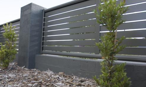 Dark Colorbond slat topper mounted above a block wall with gravel and planting below