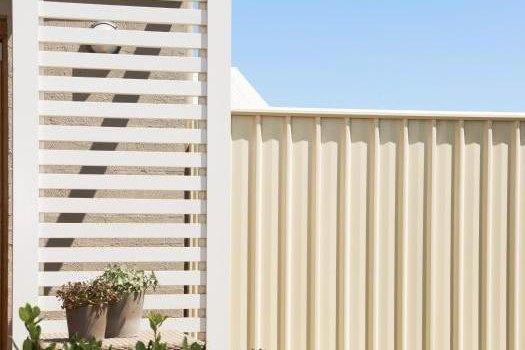 Cream Colorbond steel fence with a matching white slat screen, planting and a pot in the foreground